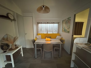 A compact room with a dining table, chairs, a hanging light fixture, a window with curtains, and a door. - Magnificent mobile home (Messanges)