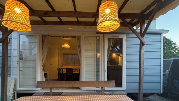 A covered outdoor seating area with a checkered tablecloth, two hanging lamps, and a wooden bench. - Magnificent mobile home (Messanges)