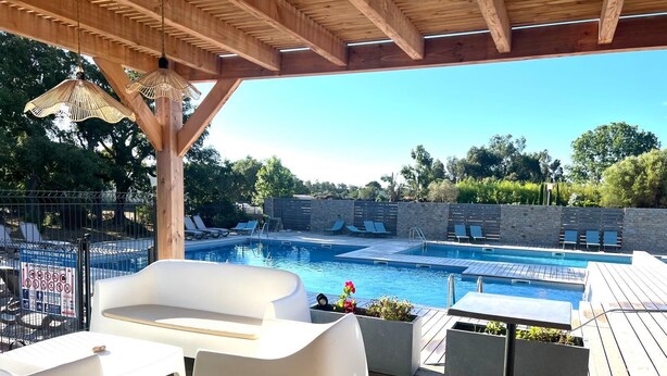 Una terrazza in legno con piscina, poltrona relax e zona salotto coperta.