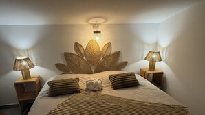 Un letto rifatto con cura, una testiera decorata con un motivo a foglie, due lampade da comodino e una coperta con trama decorativa.