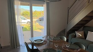 Zona pranzo con tavolo in legno apparecchiata per quattro persone, una scala e vista su un'auto e del verde all'esterno.