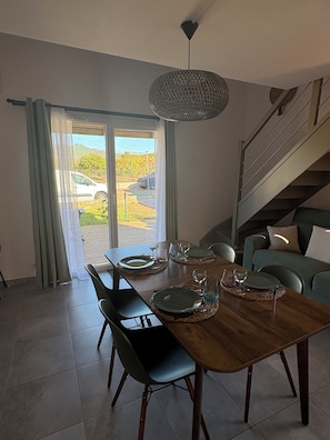 A dining area with a wooden table set for four, a staircase, and a view of a car and greenery outside. - House in hotel complex with 3 large swimming pools 5 minutes from the sea (Lecci)
