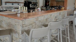 Un'area bar con un bancone in pietra, sgabelli bianchi e un lampadario.