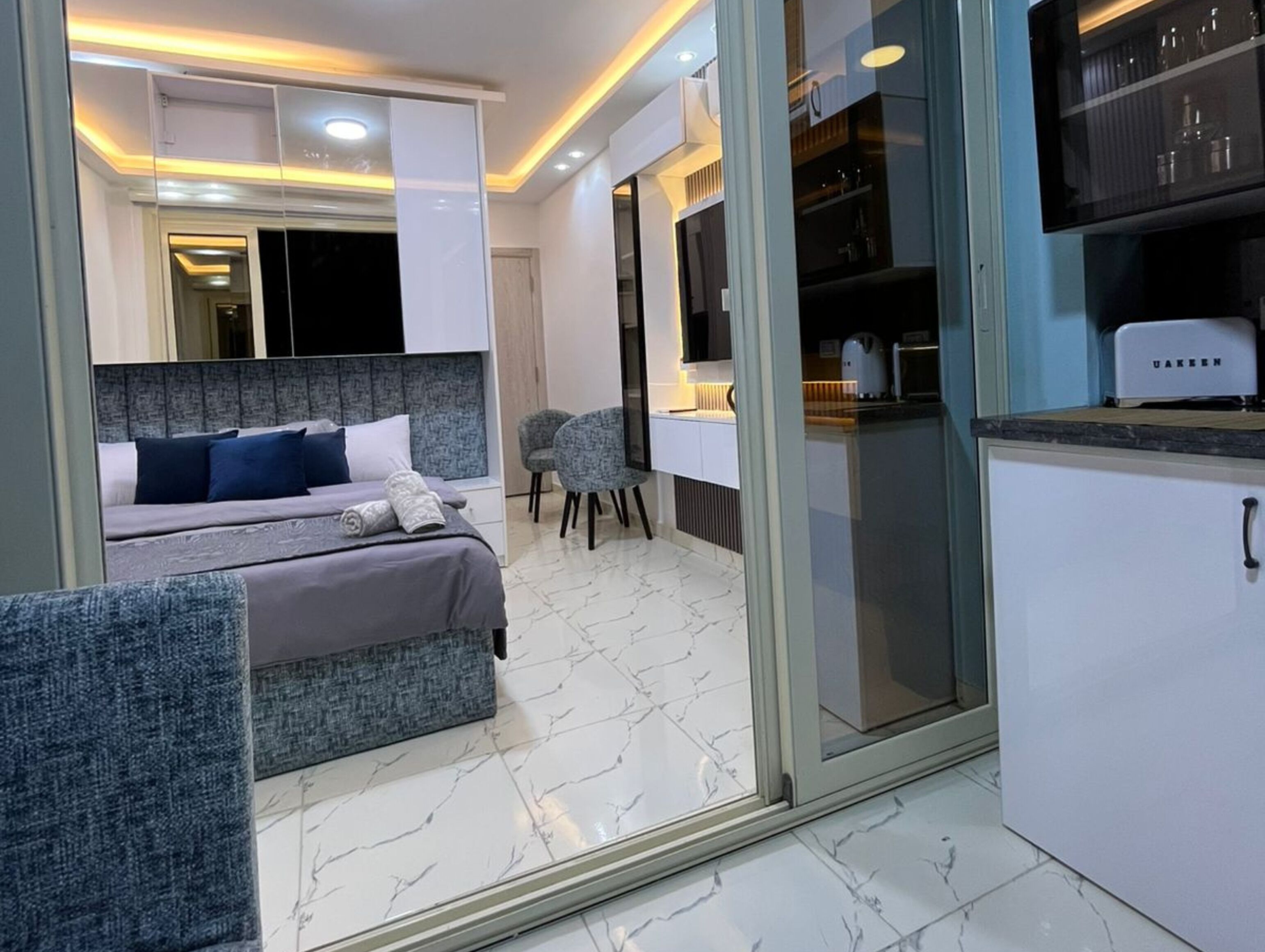Quarto moderno com cama, uma cadeira e um espaço com cozinha.