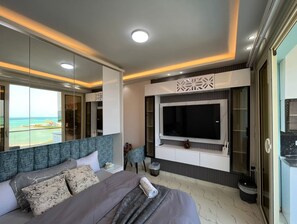 Ein modernes Schlafzimmer mit einem großen Bett, einem an der Wand montierten Fernseher und Blick auf den Ozean.