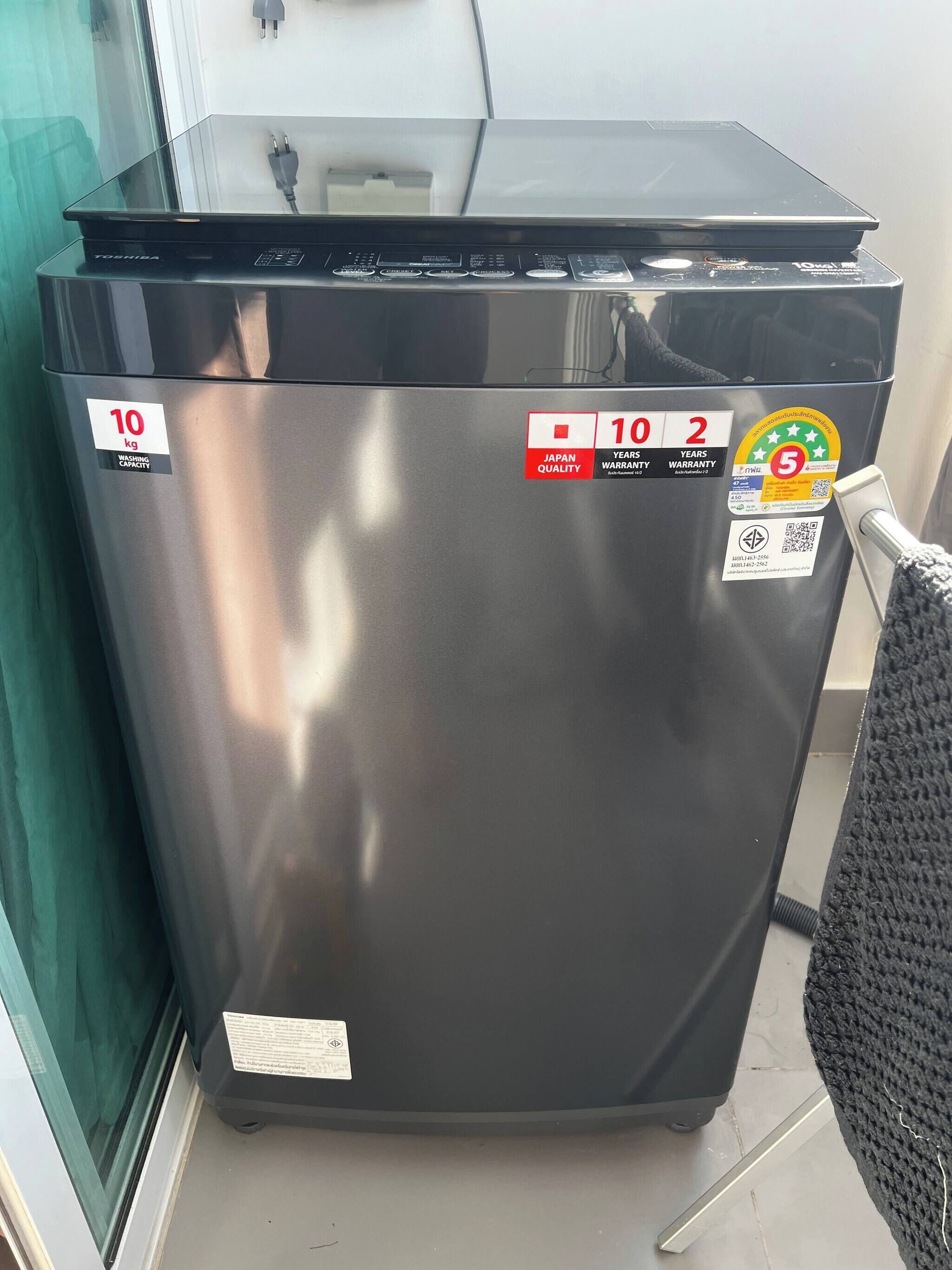 A compact, stainless steel washing machine with a capacity of 10 kg, Japanese quality and 2-year warranty stickers, and a QR code for additional information.