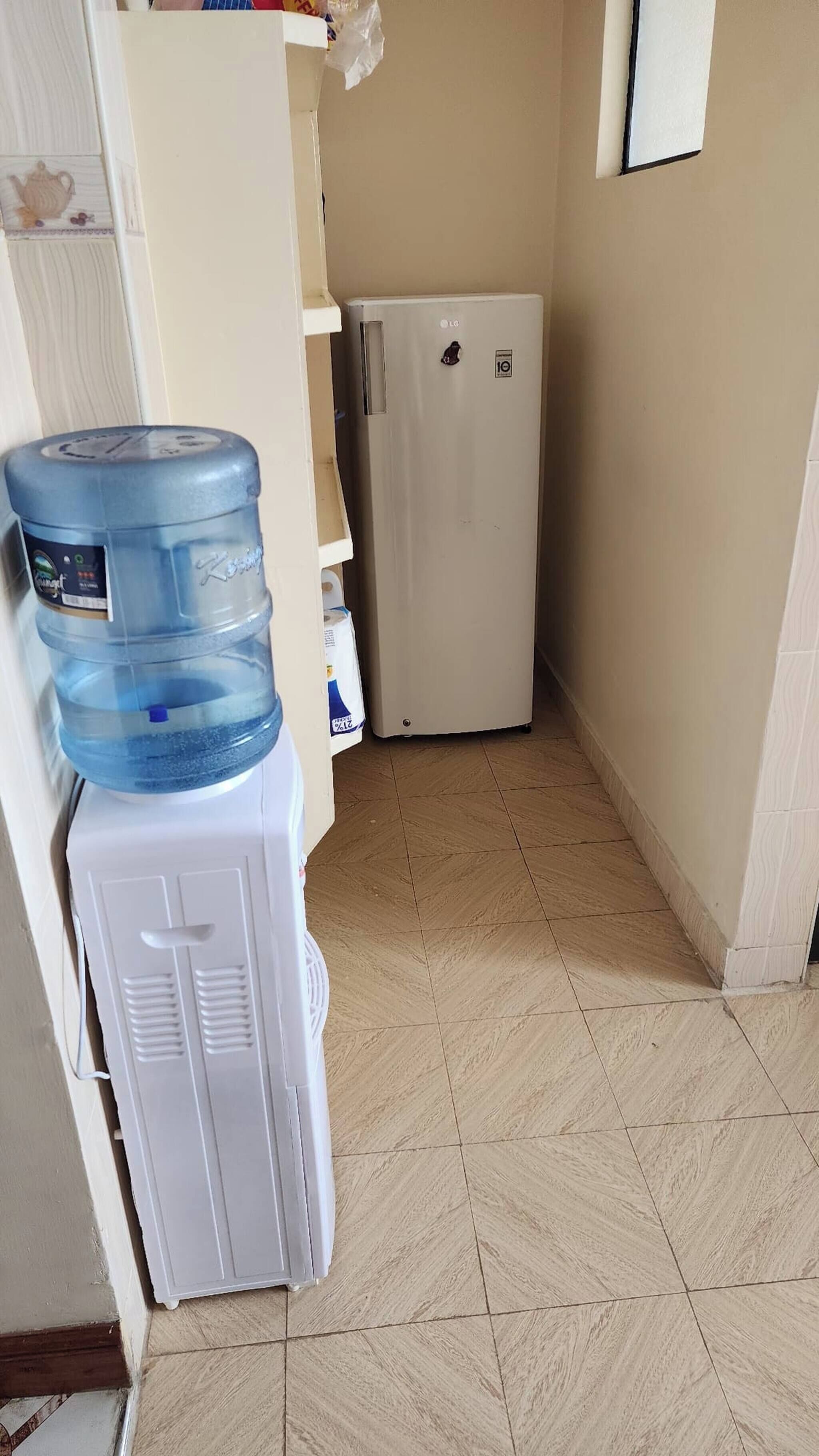 Un dispensador de agua, un refrigerador blanco y un piso de baldosas en un pasillo estrecho.