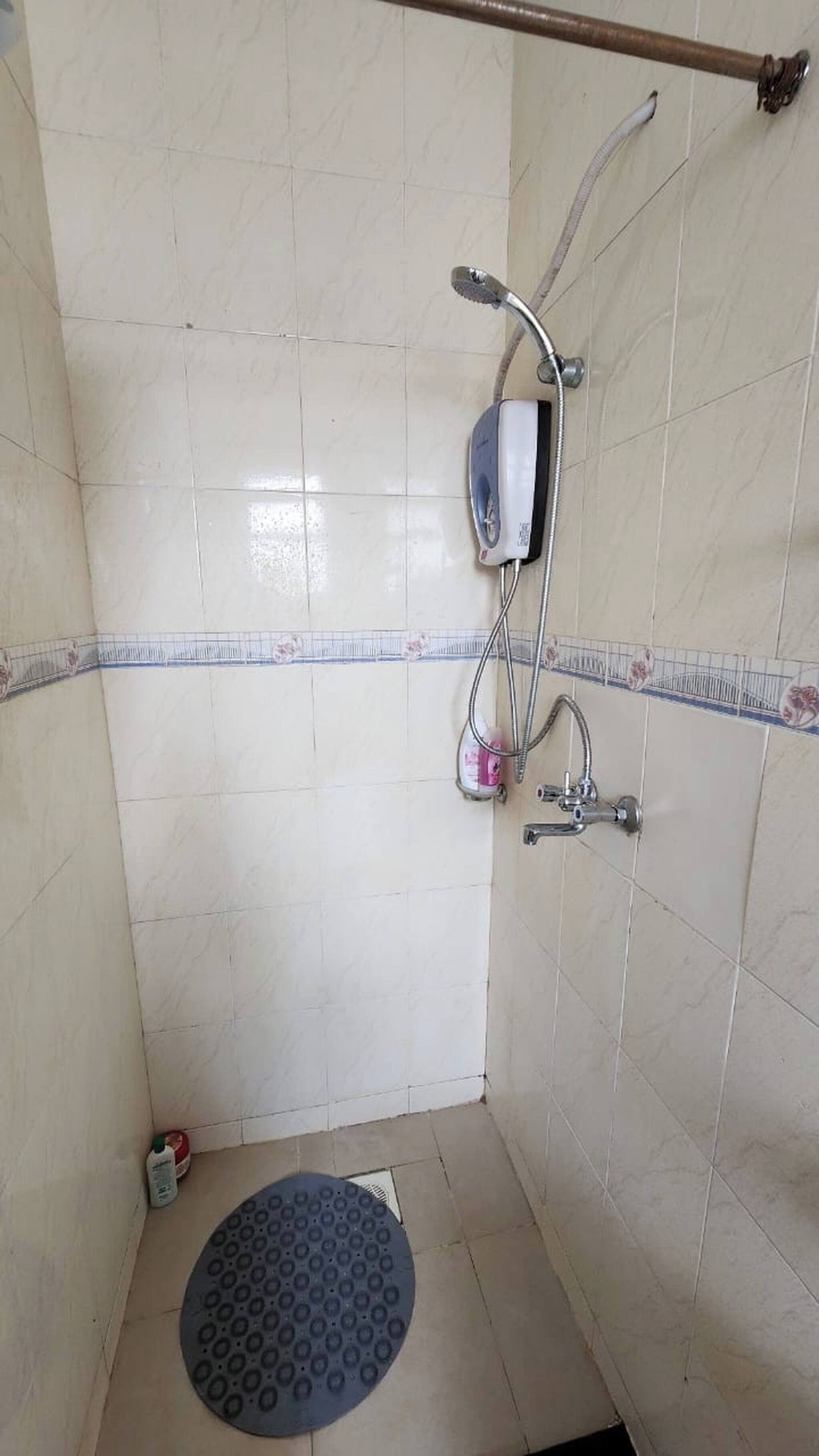 A small, tiled shower room with a handheld showerhead, a handheld soap dispenser, and a shower caddy.