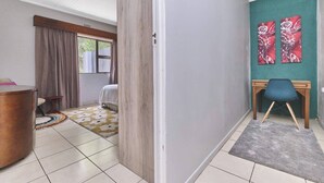Una habitación con una cama, un escritorio y una silla. Hay una ventana con cortinas, una alfombra y una pared con dos cuadros.