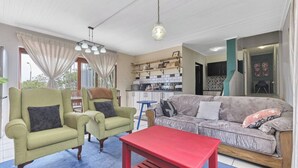 Una sala de estar con sofá, dos sillones, una mesa roja y una cocina con estantes y estufa.