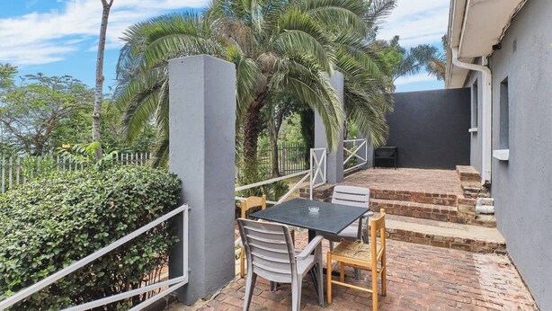 Un patio con mesa y sillas, rodeado por una valla y palmeras.