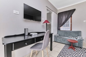 Ein modernes Zimmer mit Schreibtisch, Stuhl, Fernseher, Sofa und kleinem Tisch.