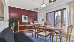 A living room with a sofa, dining table, chairs, a small cabinet, and a window with a view.