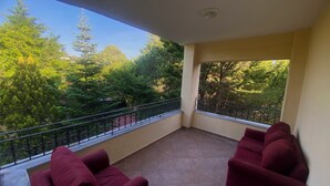 A balcony with two red sofas, a tiled floor, and a view of trees and a clear sky. - Goat house near the airport (Arnavutköy)
