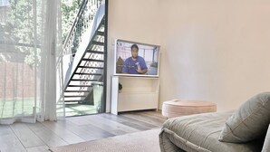 Ein modernes Wohnzimmer mit einer Couch, einem Fernseher, einer Treppe und Blick ins Freie.