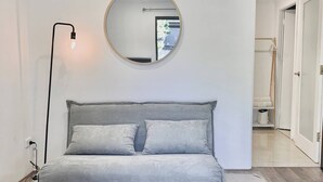 Ein modernes Wohnzimmer mit einem grauen Sofa, einem runden Spiegel, einer Stehlampe und einem weißen Hocker.