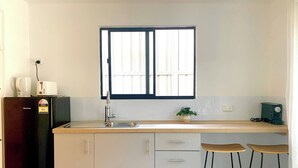 Eine Küche mit Kühlschrank, Spüle, Fenster und Barhocker.