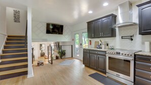 A modern kitchen with dark cabinets, a stainless steel oven, and a wooden staircase. - GREEN LANTERN: Game Room, Furnished Deck, Modern (Lexington)
