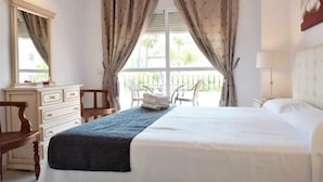 A hotel room with a bed, a dresser, a chair, a table, and a window with curtains. - Villa Anna - 4 Bedrooms F-3 (Marbella)