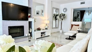 A modern living room with a fireplace, white sofas, a flat-screen TV, and decorative plants. - Villa Anna - 4 Bedrooms F-3 (Marbella)