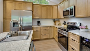 A modern kitchen with stainless steel appliances, wooden cabinets, and a large window. - Margaritaville Access! Luxe Ozark Oasis w/ Hot Tub (Osage Beach)