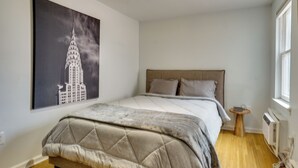 Ein Schlafzimmer mit einem Bett, einem kleinen Nachttisch, einem Heizkörper und einem Fenster.