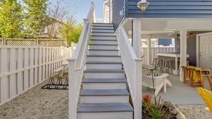 Eine Treppe führt zu einer Veranda mit Gartenmöbeln und einem weißen Zaun.