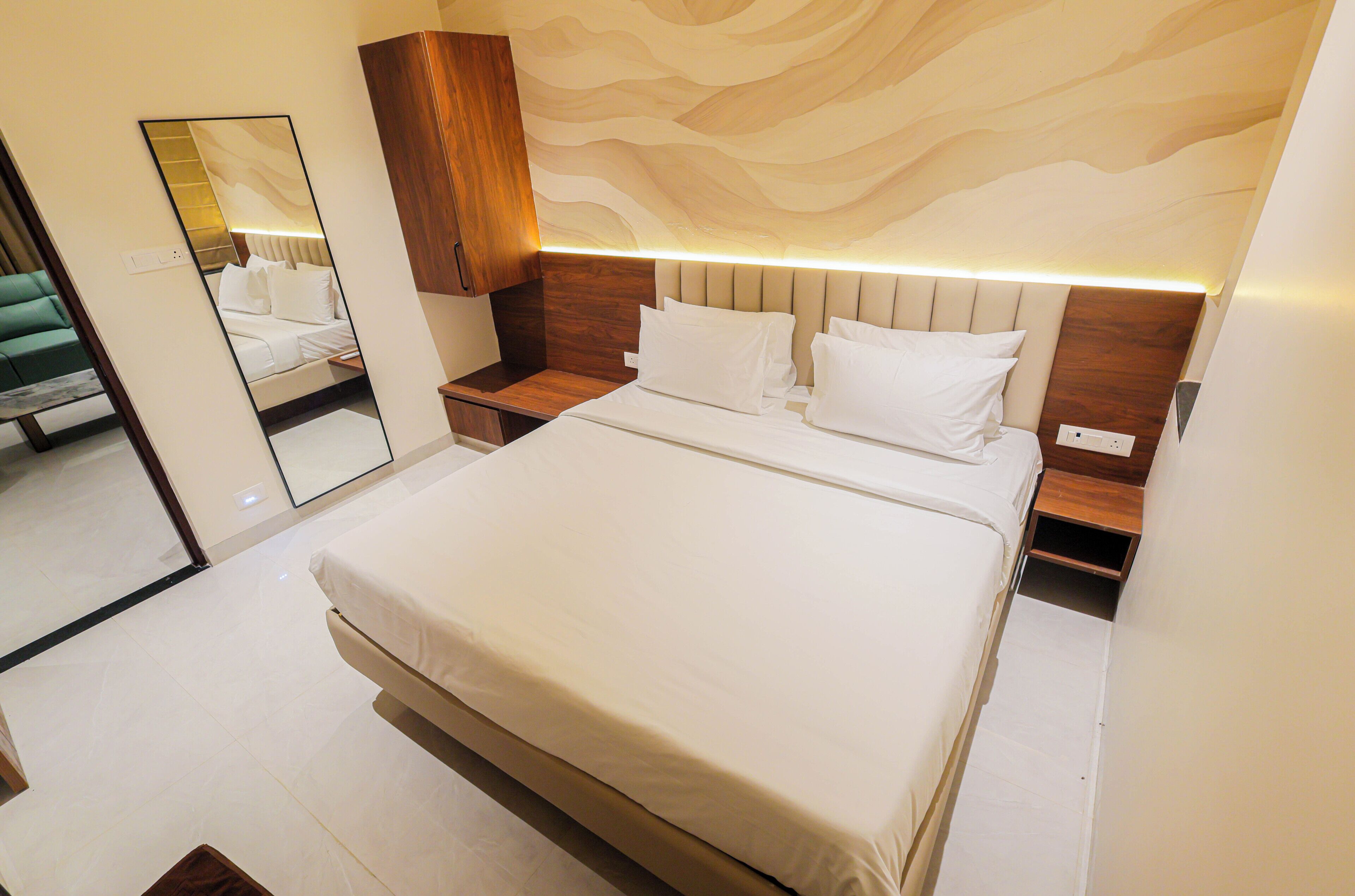 A modern bedroom with a large bed, wooden headboard, bedside tables, and a mirror.