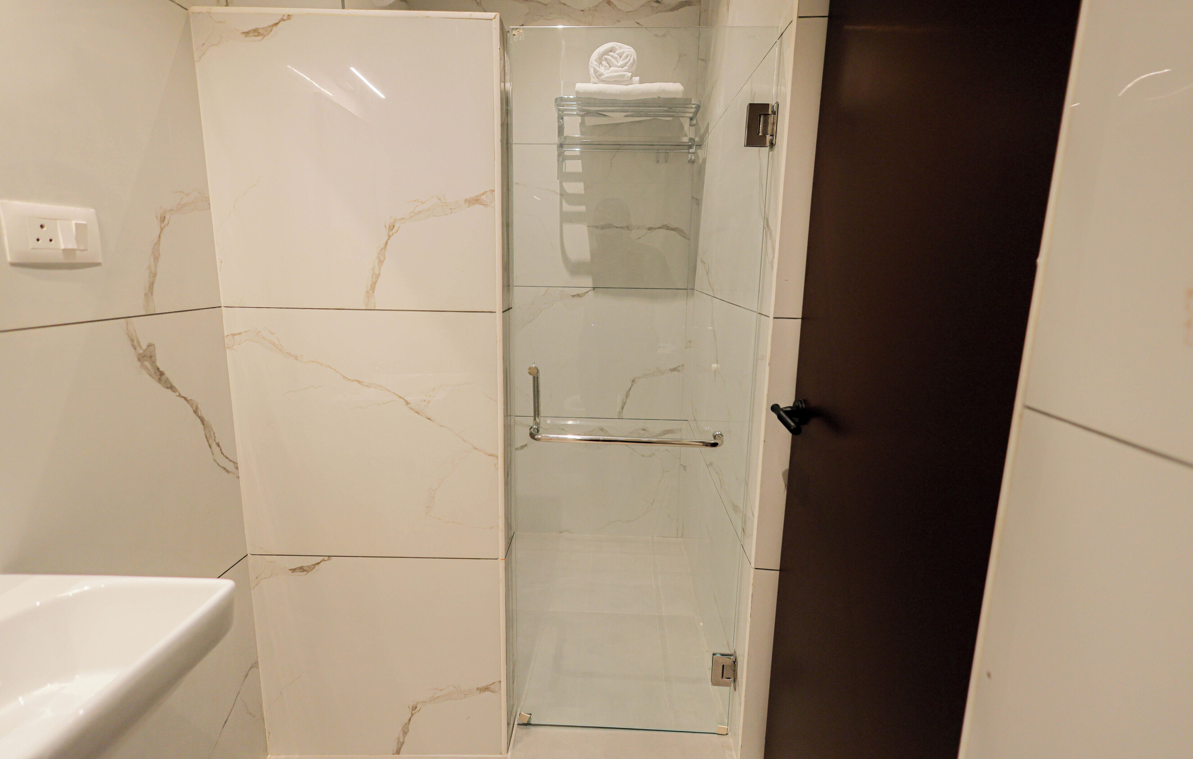 Un baño con cabina de ducha de vidrio, un inodoro blanco y un revestimiento de pared con diseño de mármol.