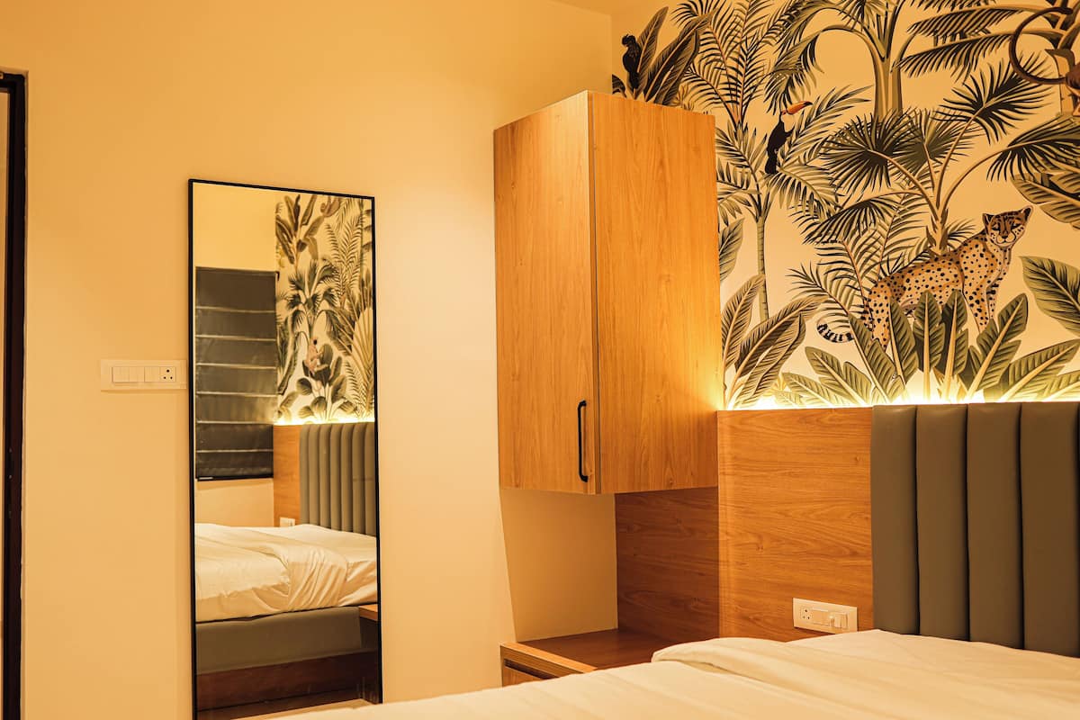 A hotel room with a bed, a wooden wardrobe, a mirror, and a wall with a tropical mural.