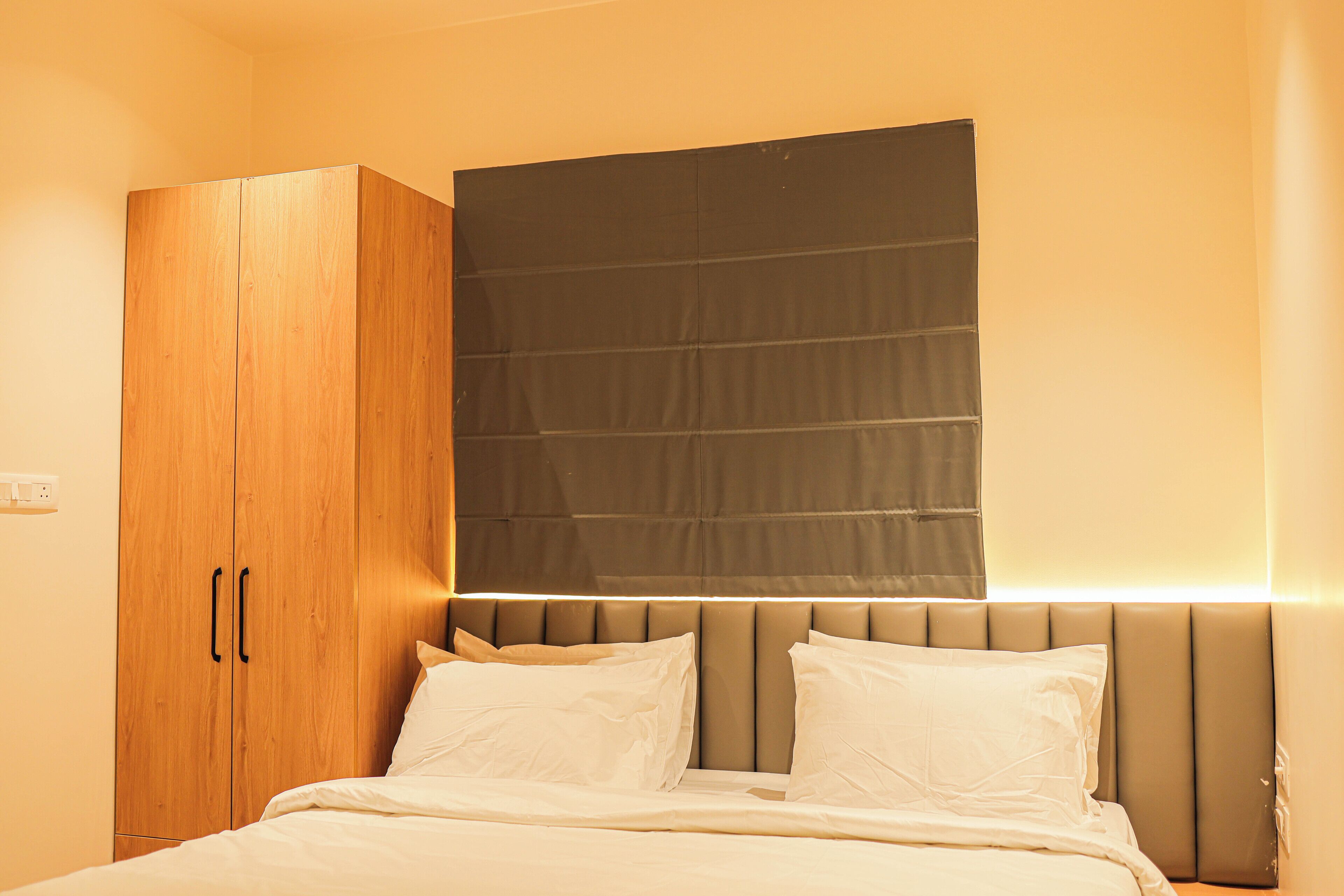 A bedroom with a bed, a wardrobe, and a headboard with built-in lighting.
