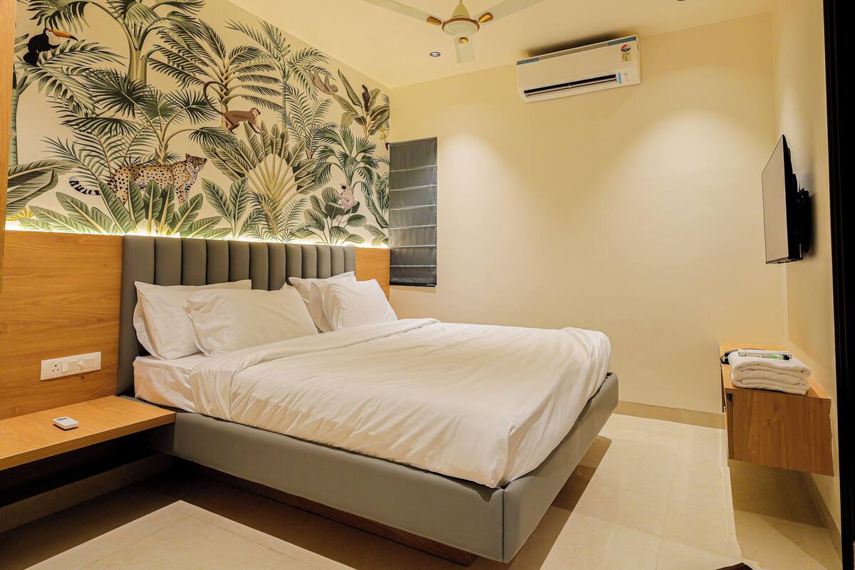 A modern bedroom with a bed, bedside tables, a wall-mounted air conditioner, and a decorative mural.