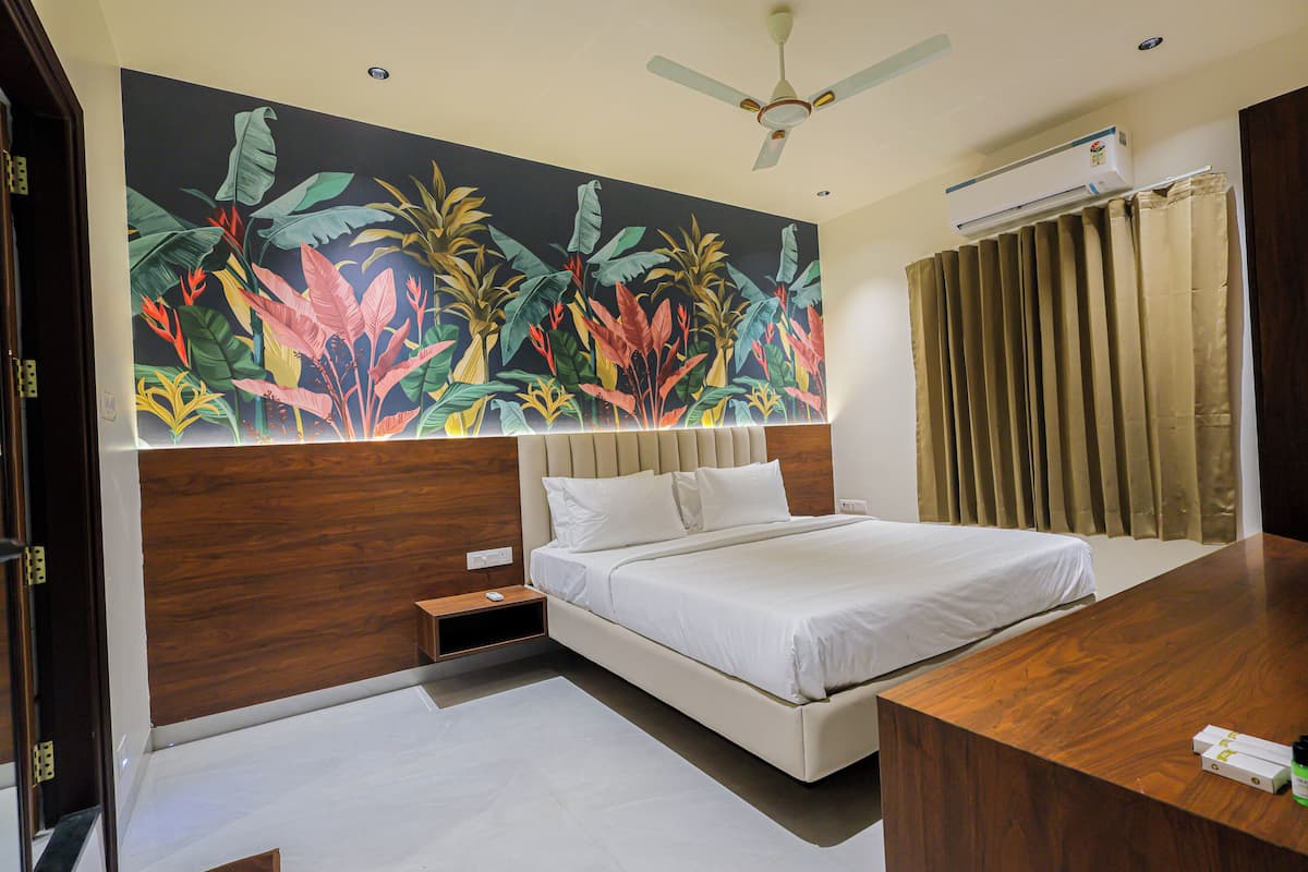 A hotel room with a bed, bedside table, a desk, a ceiling fan, and a large tropical mural on the wall.