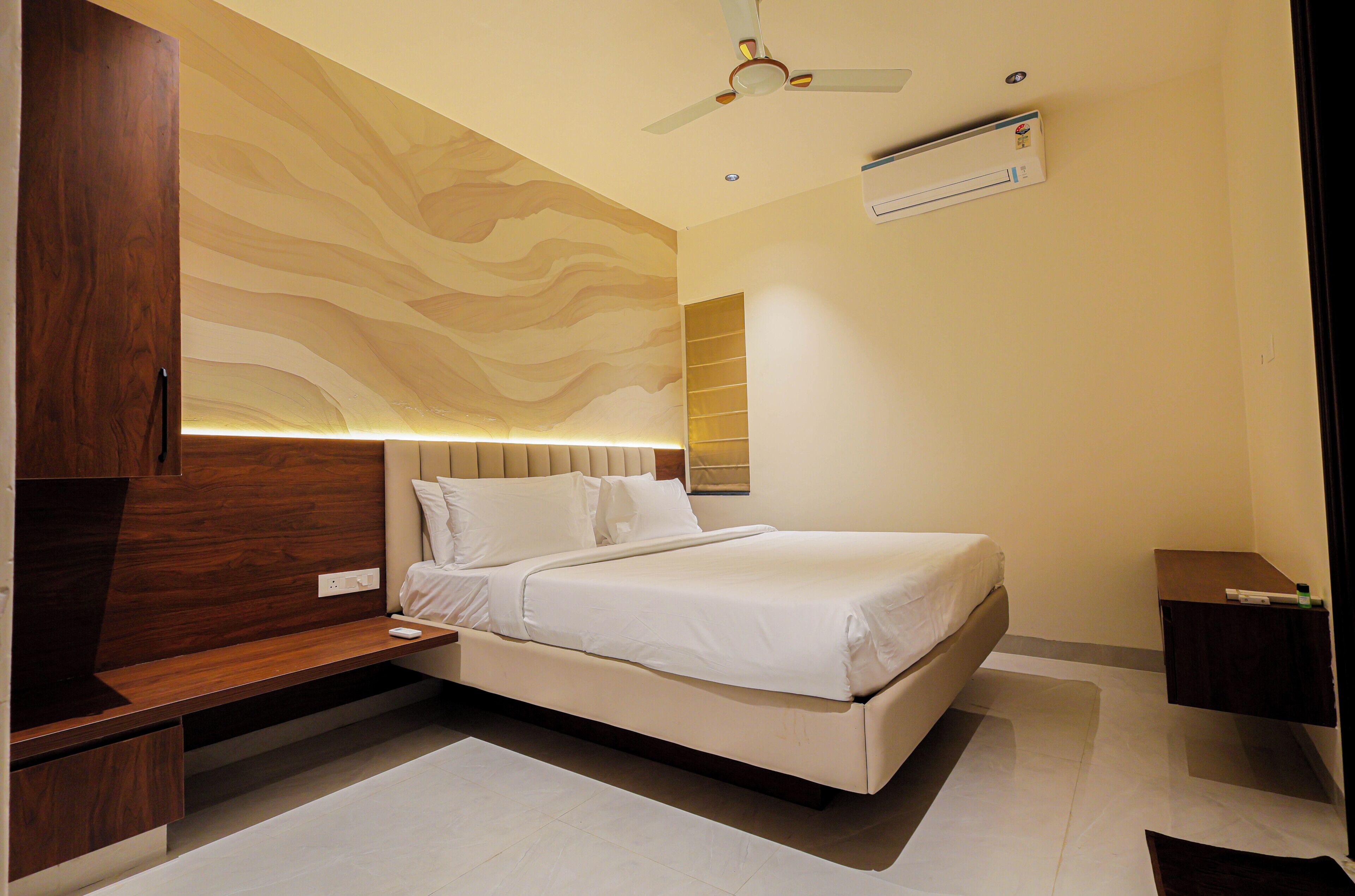 A bedroom with a bed, wooden wardrobe, ceiling fan, air conditioning unit, and a bedside table.