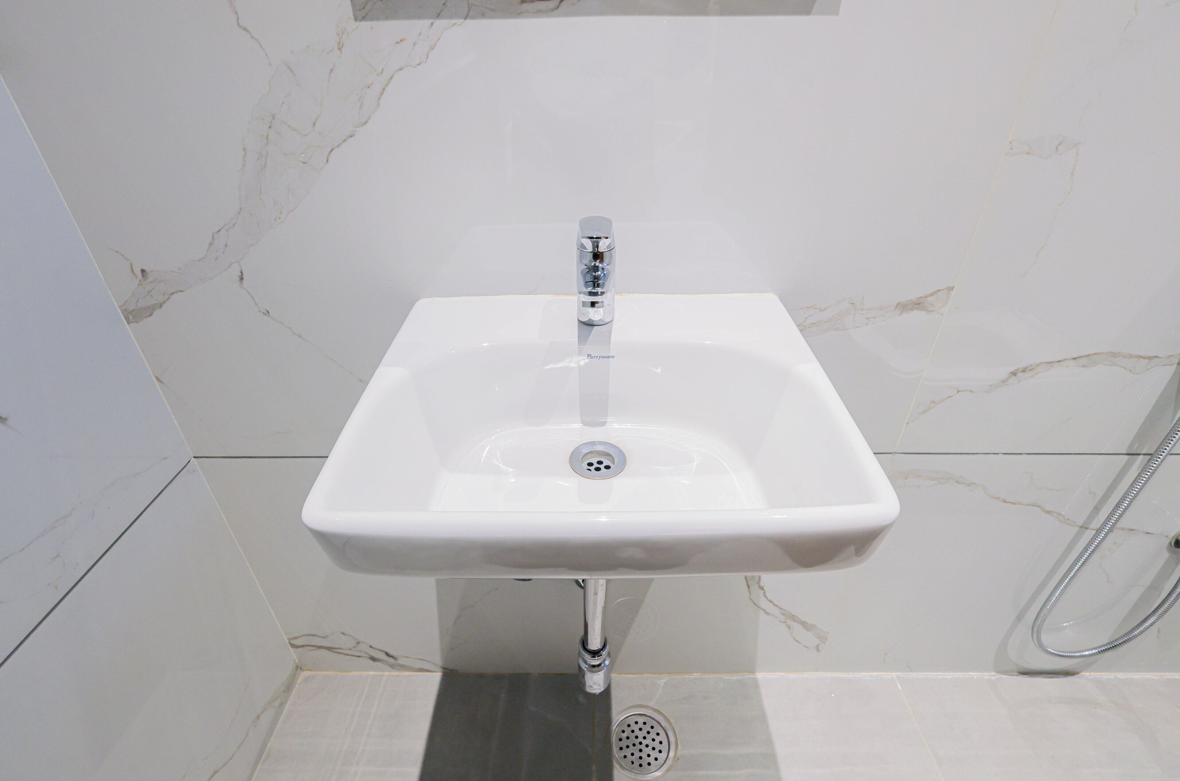 Une salle de bain avec un lavabo blanc, une douche et un mur décoré d’un motif imitant le marbre.