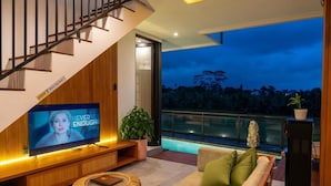 A modern living room with a TV, sofa, and staircase. - Paz Tropical Villa Ubud (Ubud)