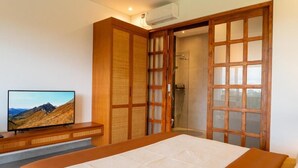 A bedroom with a bed, a TV on a wooden console, a sliding door leading to a shower, and a view of a mountain. - Paz Tropical Villa Ubud (Ubud)