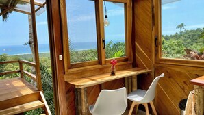 A wooden room with a view of the ocean, a table, two chairs, and a hanging light bulb.