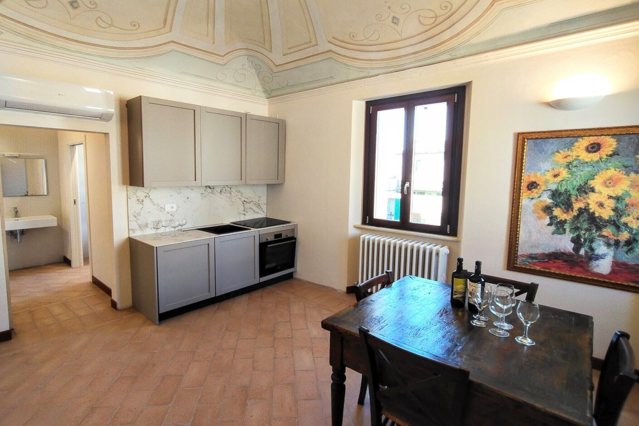 Una cucina con fornello, forno e pensili, un tavolo da pranzo con sedie, una finestra con vista e un quadro appeso al muro.