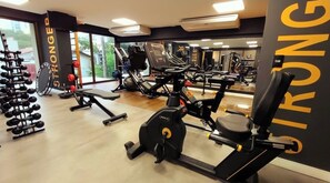 Ein Fitnessstudio mit verschiedenen Trainingsgeräten, einer Spiegelwand und einem motivierenden Schild mit der Aufschrift 'STRONGER'.