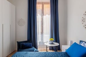 A bedroom with a bed, a small round table with a vase, and a nightstand with a lamp. - A comfortable and charming 40 square meters apartment, perfect for three people, located on the second floor of a period building with an elevator (NOT accessible to disabled guests).The property is located near Rome Termini Station and the Castro Pretor (Rome)