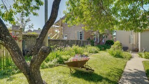 Un jardin avec une brouette, un arbre et une maison dont la façade est en briques.