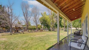 A covered patio with a concrete floor, a metal bench with pillows, and a view of a grassy yard and trees. - Private Acreage, Pet-Friendly Yard! Gilbert Haven (Gilbert)