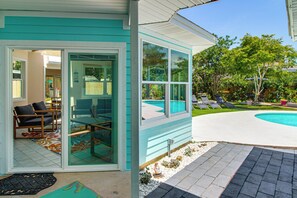 Ein Haus mit Glastür, das auf eine Terrasse mit Pool, Gartenmöbeln und Garten führt.