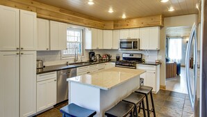 Cucina con mobili bianchi, isola centrale, elettrodomestici in acciaio inossidabile e soffitto in legno.