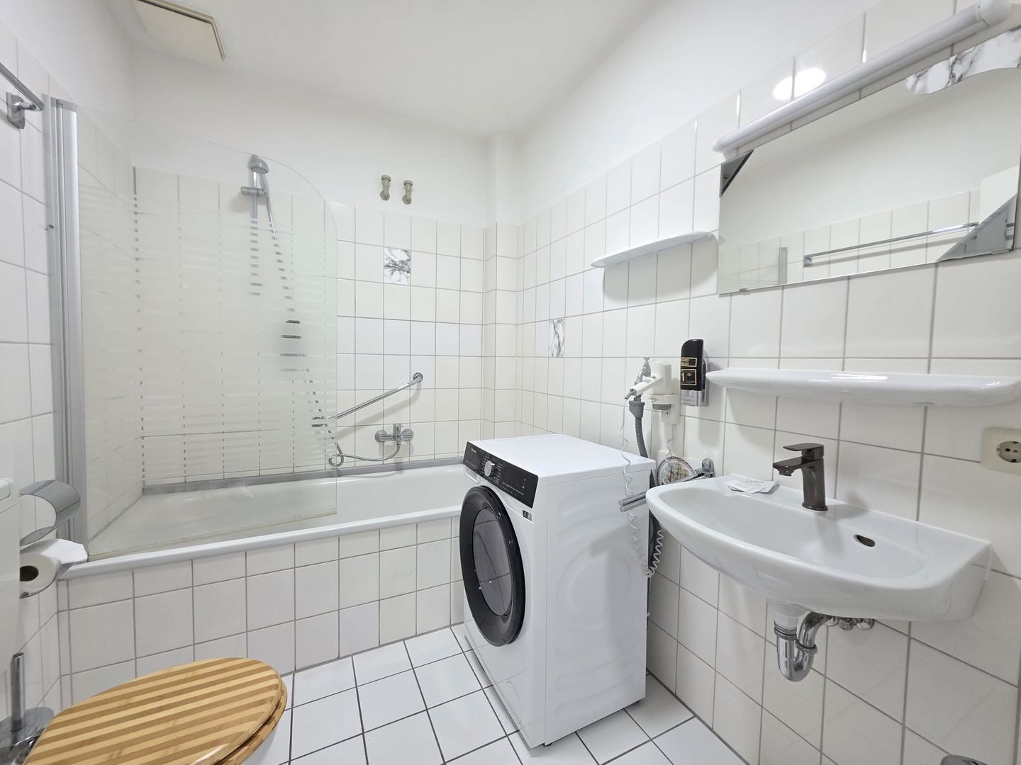 Ein modernes Badezimmer mit Dusche, Waschmaschine, Waschbecken und Toilette.