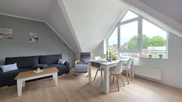 A modern loft apartment with a dining area, a sofa, and a large window.