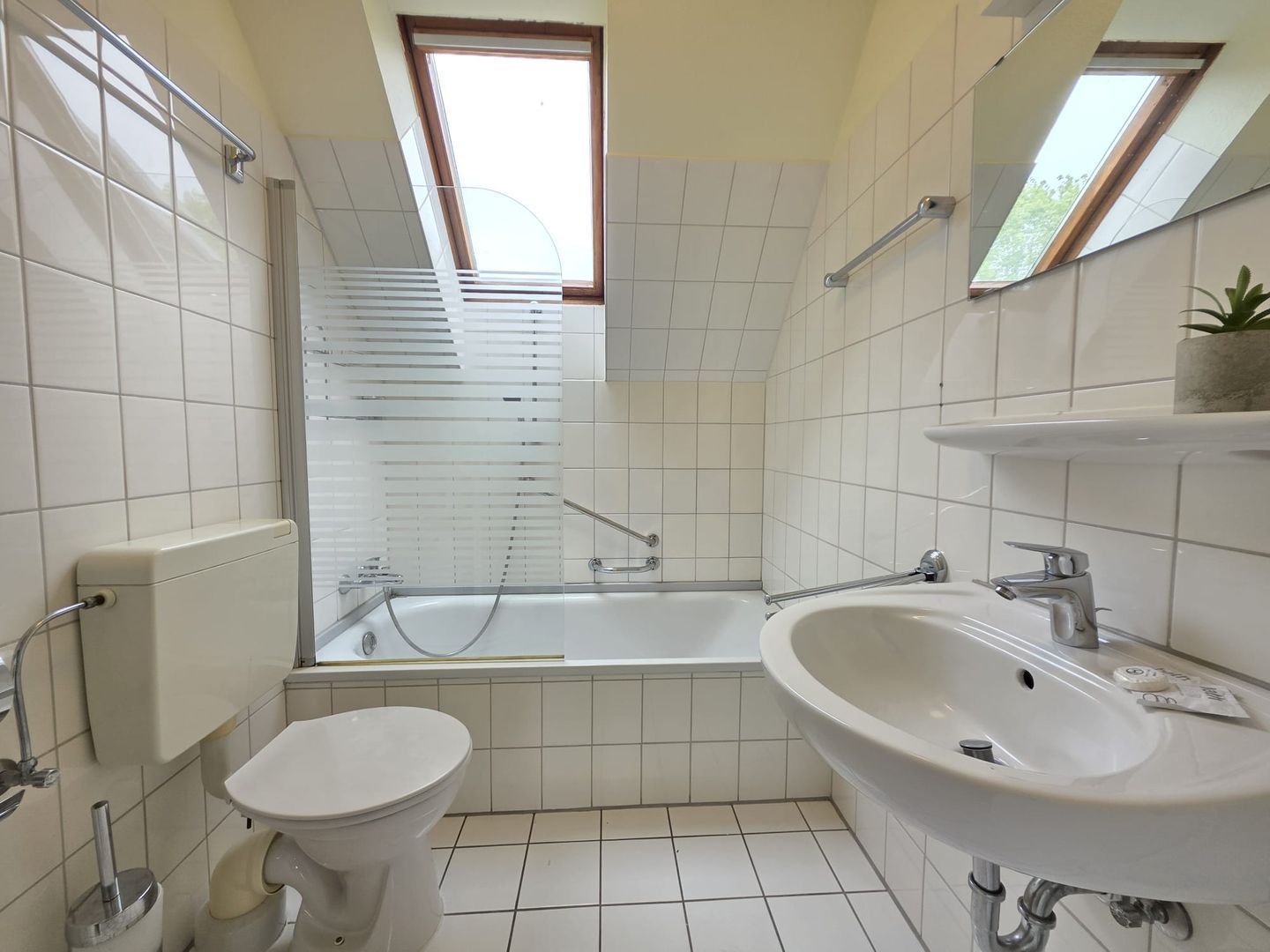 Baño con inodoro, lavamanos, bañera y tragaluz.