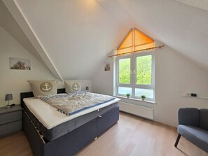 Un dormitorio con cama, ventana con vistas, radiador y una silla.