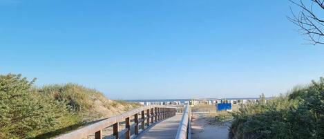 A wooden boardwalk leading to a beach with dunes and sparse vegetation.